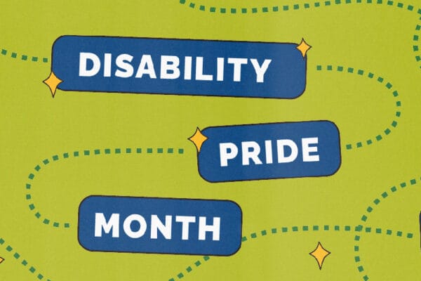 A baby photo of Mark, in a bathroom, posing with his arm on his hip and his other arm on his shoulder with his legs crossed and inverted. He has short black hair and is wearing black shorts, a navy and pink shirt, and black shoes.