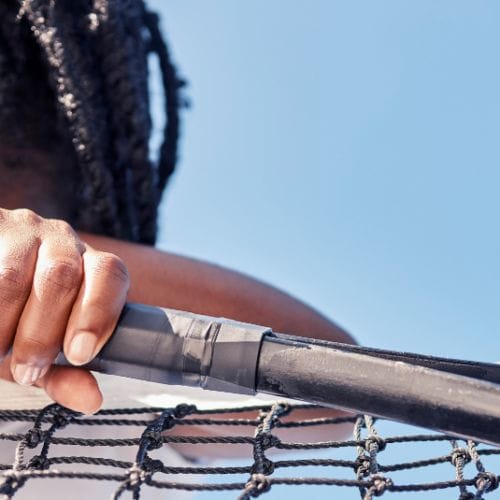 Image of a tennis player holding a racket with their head down, leaning on a net on a tennis court.