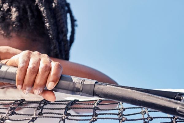 Image of a tennis player holding a racket with their head down, leaning on a net on a tennis court.