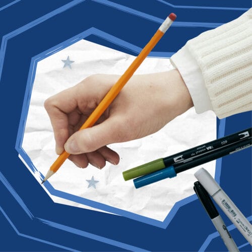 Hand writing on paper with pens and markers nearby.