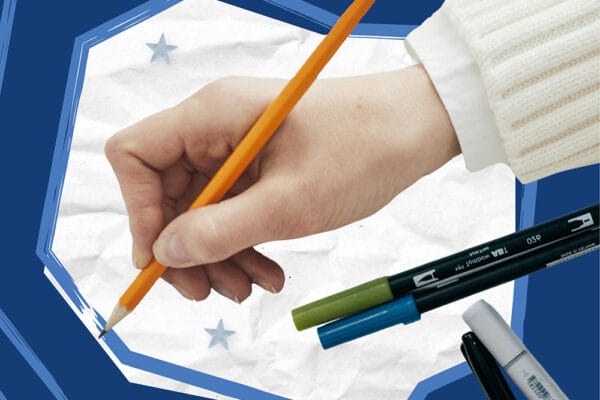 Hand writing on paper with pens and markers nearby.