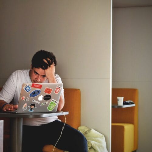 Young person sitting at a laptop holding their head