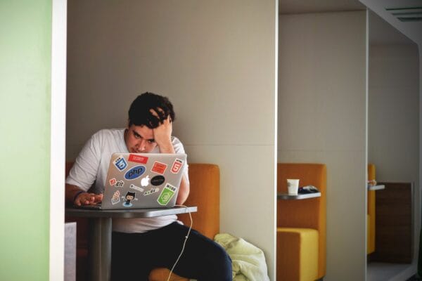 Young person sitting at a laptop holding their head